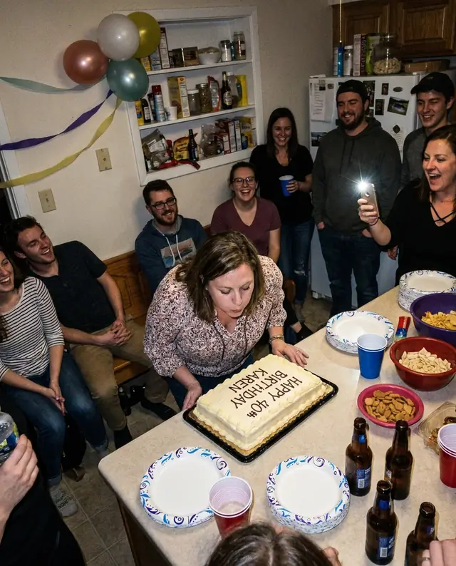 Friends crowding around a kitchen bench as she blows out her 40th birthday candles